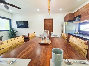 A dining area with a wooden table, chairs, a television, and a kitchen area with a refrigerator and microwave. - Luxury Boutique Hotel Villas Jardin Caracol Tulum (Tulum)