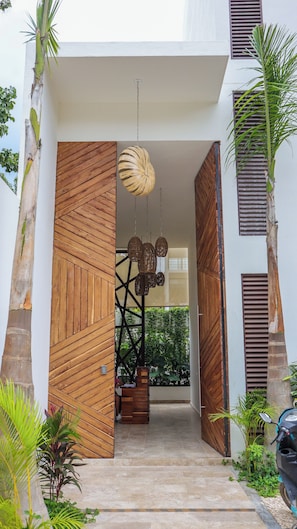 A modern entrance with wooden paneling, a hanging light fixture, and a staircase leading to a covered area with plants.