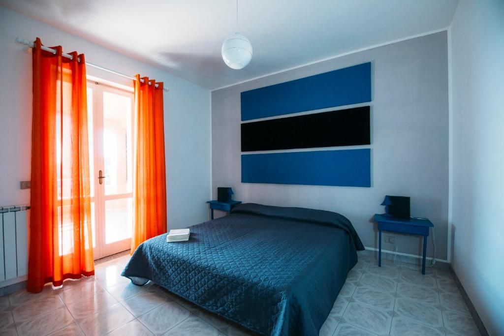 Ein Schlafzimmer mit Bett, Nachttisch, Lampe und einem Fenster mit Vorhängen.