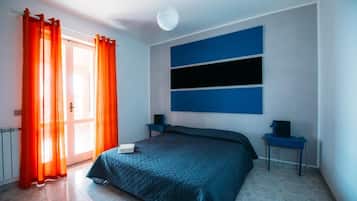 Ein Schlafzimmer mit Bett, Nachttisch, Lampe und einem Fenster mit Vorhängen.