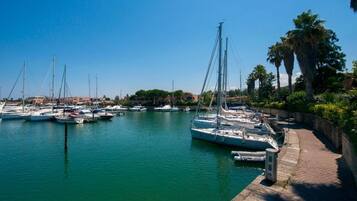 Ein Yachthafen mit mehreren Segelbooten, die an einer gepflasterten Uferpromenade liegen, umgeben von Grünflächen und Gebäuden im Hintergrund.