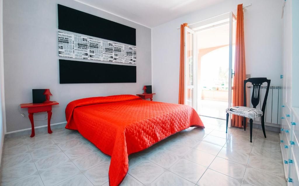 Una camera da letto con un letto grande, una coperta rossa, una lavagna con scritte, un comodino rosso, una sedia e una finestra con tende.