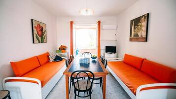 Ein Essbereich mit einem langen Tisch, orangenen Kissen und Stühlen.