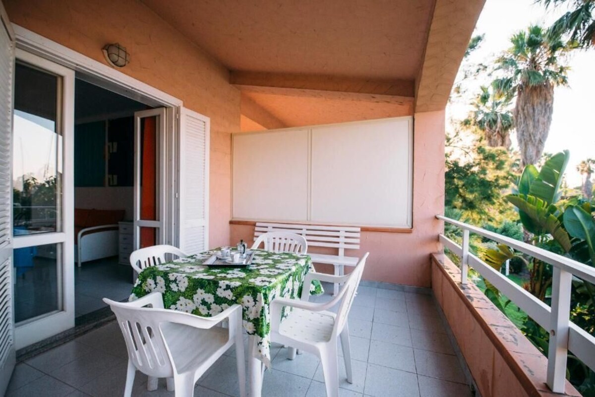 Un balcon avec une table et des chaises, une porte coulissante et une vue sur des palmiers.
