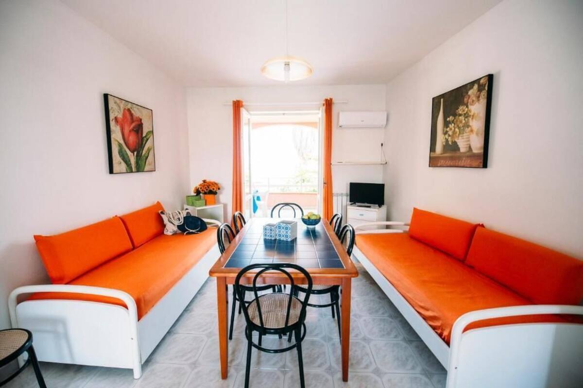 Ruokailutila, jossa on pitkä pöytä, oranssit tyynyt ja tuolit.