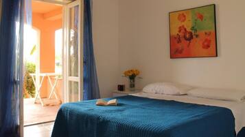Ein Schlafzimmer mit einem Bett, einem Gemälde, einer Vase mit Blumen und Blick ins Freie.