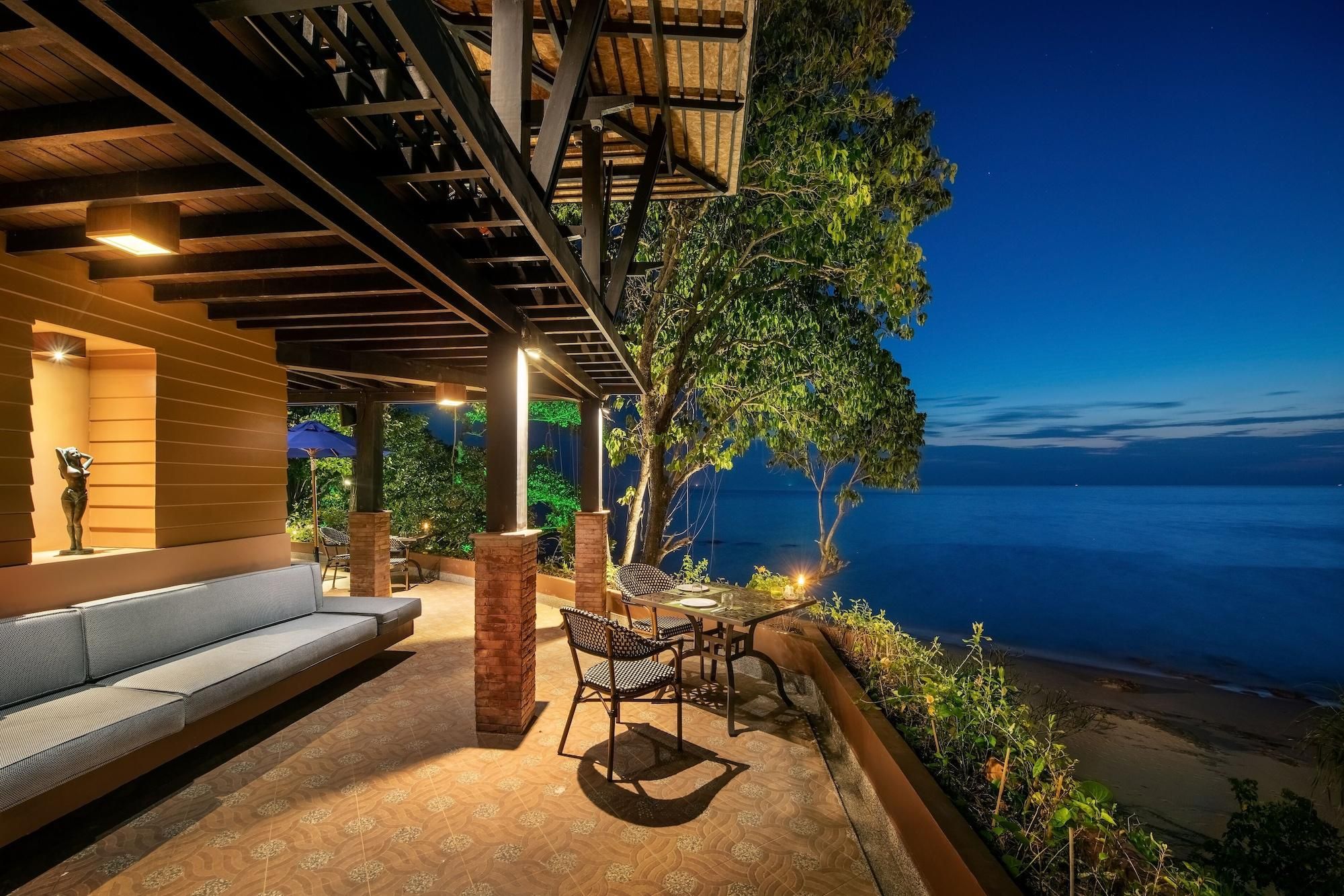 Uma área de estar externa com vista para o oceano, com um sofá, cadeiras e uma mesa.