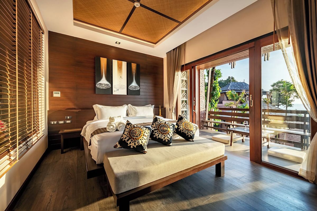 A modern bedroom with a large bed, a bench, and a balcony with a view.