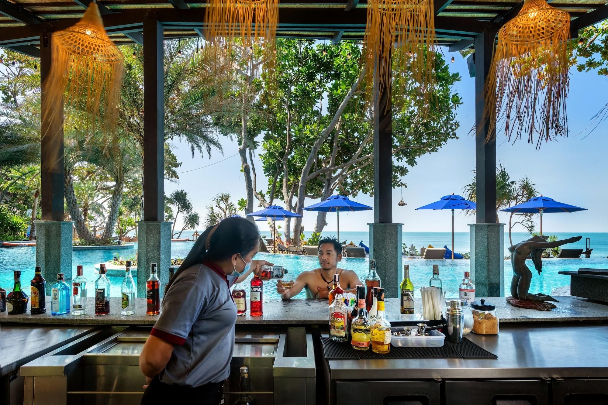Zona de bar con vista a la piscina, con taburetes y una variedad de botellas de licores.