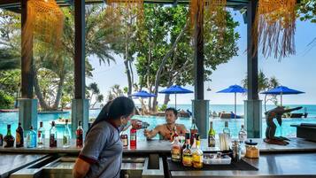 Zona de bar con vista a la piscina, con taburetes y una variedad de botellas de licores.