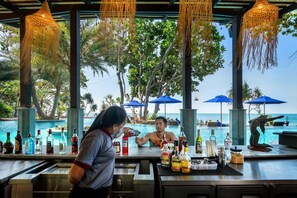 A bar area with a pool view, bar stools, and a variety of liquor bottles. - Nirvana Beach Resort (Ko Lanta)