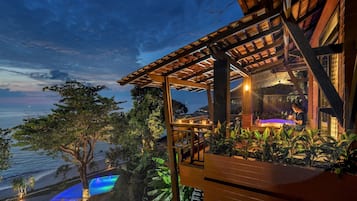 Una estructura de madera con piscina y vista al océano al atardecer.