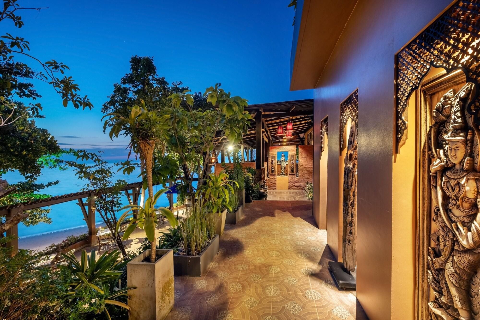 Un camino que lleva a una zona de playa con vista al océano, rodeada de vegetación exuberante y un muro decorativo con intrincados grabados.