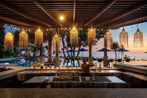 An outdoor bar area with a pool, tiki-style hanging lights, and umbrellas overlooking the sea. - Nirvana Beach Resort (Ko Lanta)