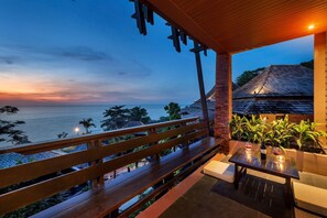 Un balcon en bois offrant une vue sur l’océan au crépuscule.