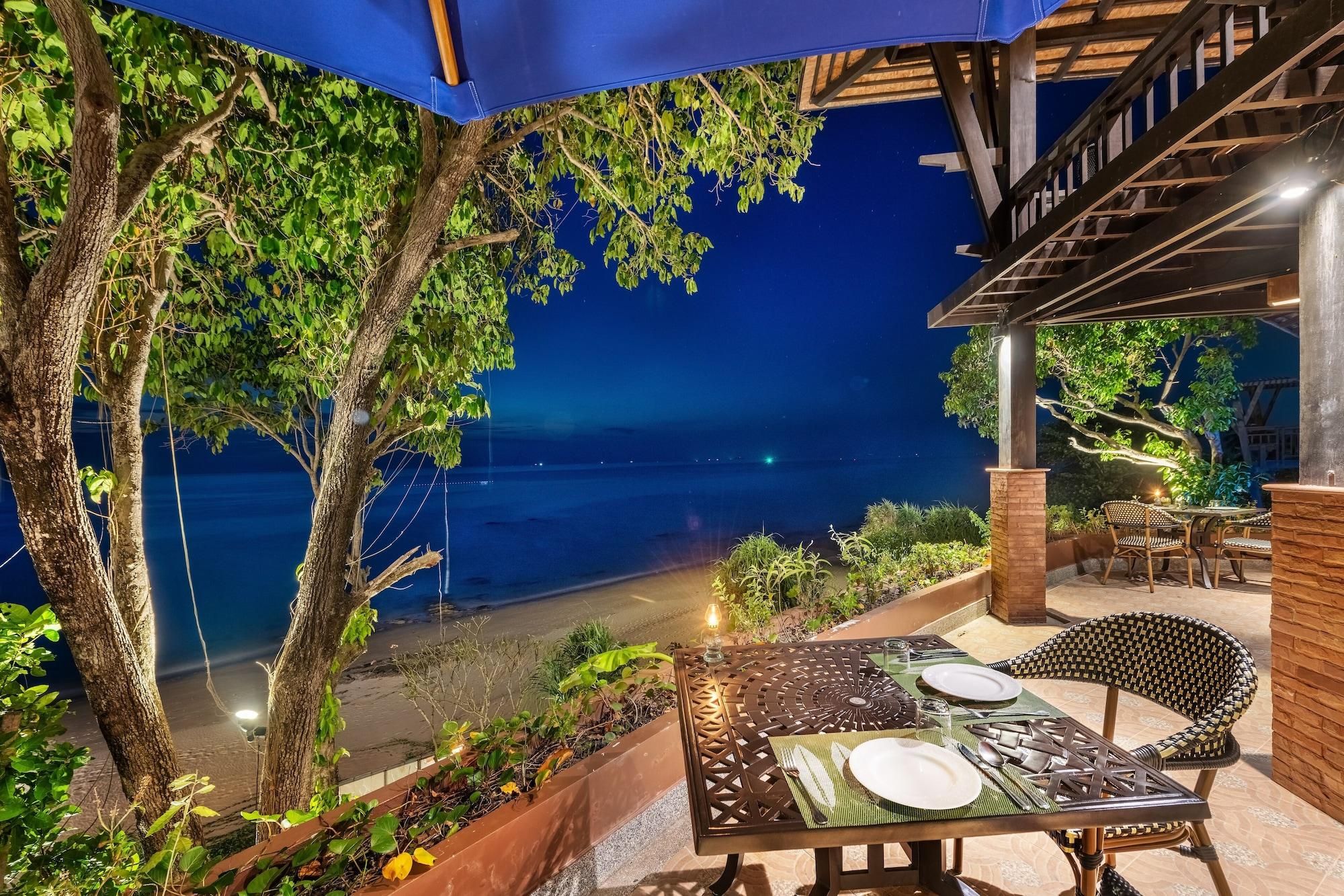 Ein Essbereich im Freien mit Tisch für zwei Personen mit Blick auf einen Strand bei Nacht.
