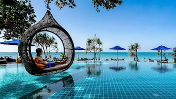 Un hombre descansando en una hamaca junto a una piscina con vistas al océano.