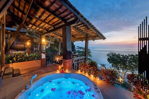 Un bain à remous agrémenté de nénuphars, une pergola en bois et une vue sur l’océan au coucher du soleil.