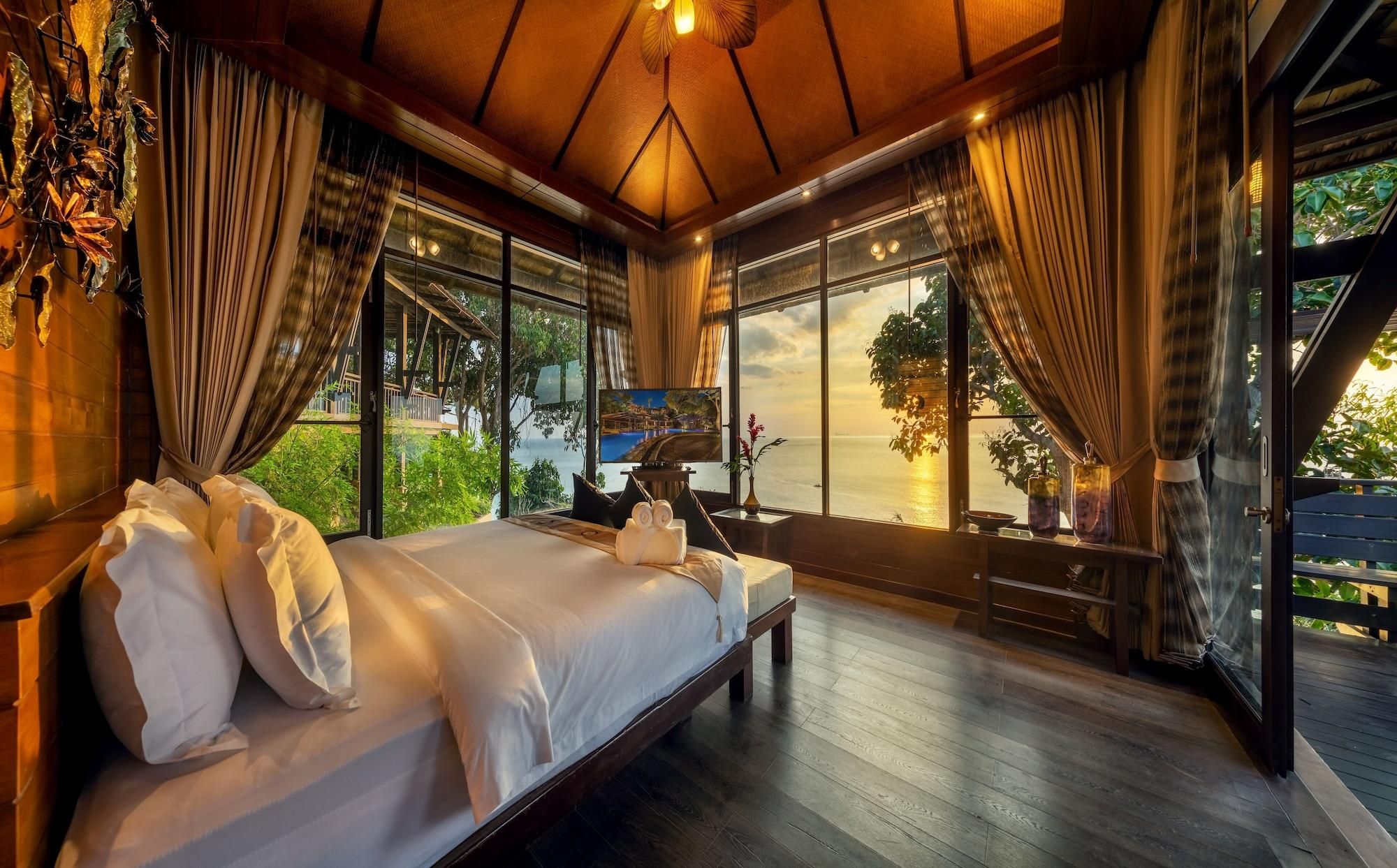 Un dormitorio amplio con una cama grande, suelo de madera y ventanas grandes con vistas al mar.