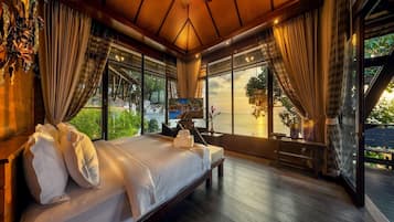Un dormitorio amplio con una cama grande, suelo de madera y ventanas grandes con vistas al mar.