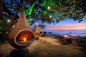 Outdoor seating areas with hanging chairs and tables, overlooking a beach at sunset. - Nirvana Beach Resort (Ko Lanta)