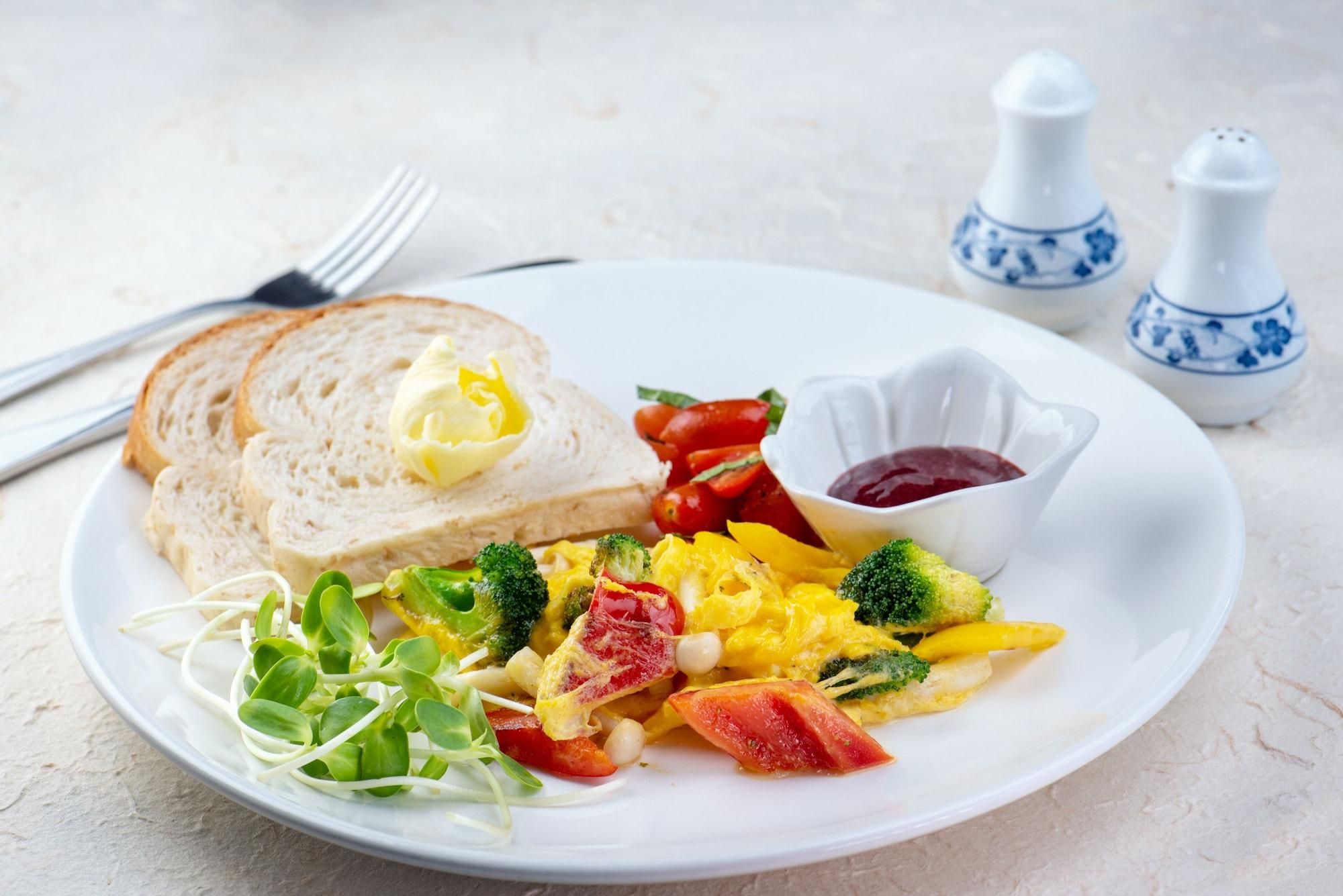 Un plato con huevos revueltos, verduras y tostadas con mantequilla.