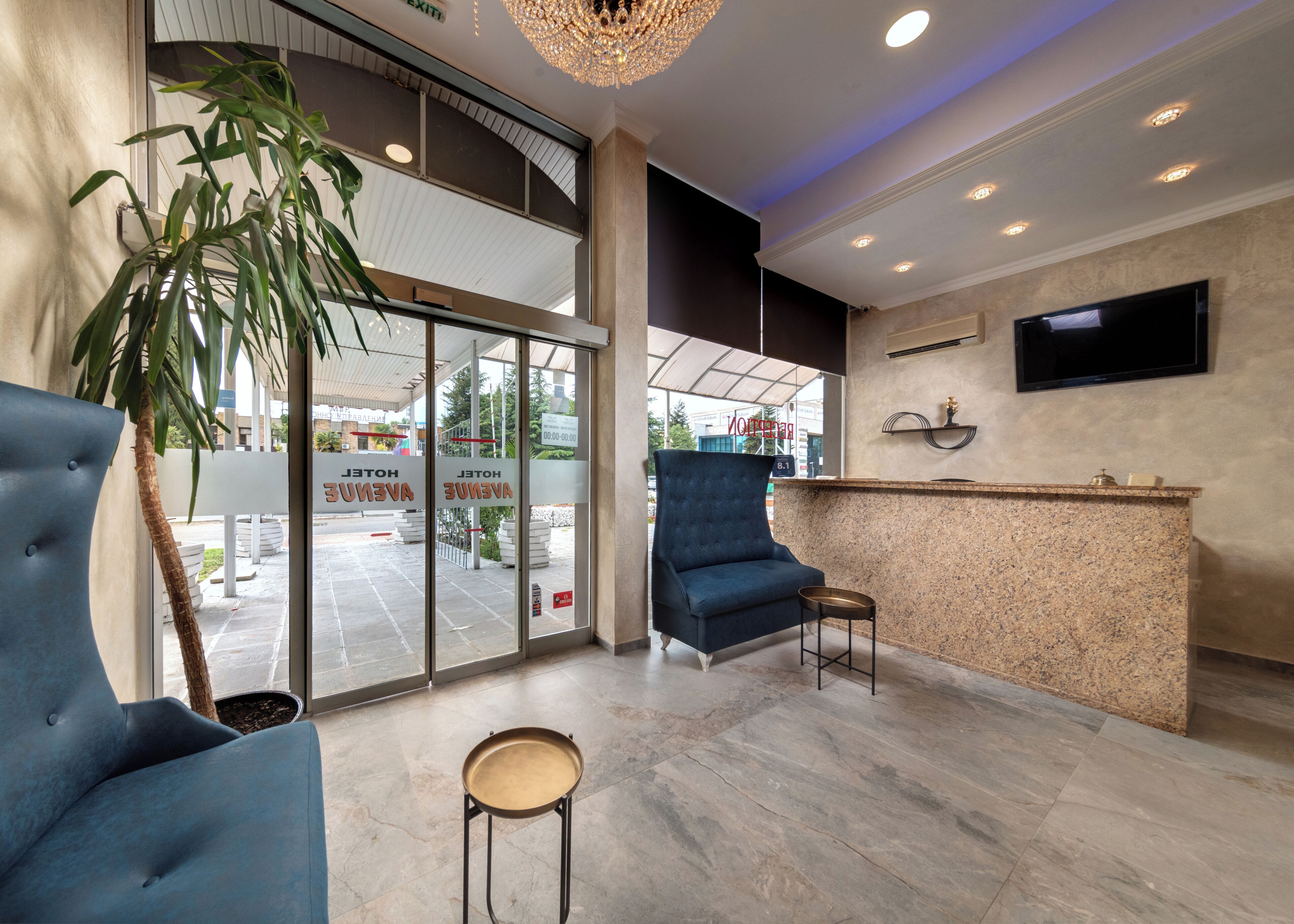 A hotel lobby with a reception desk, a blue armchair, a small round table, and a large potted plant.