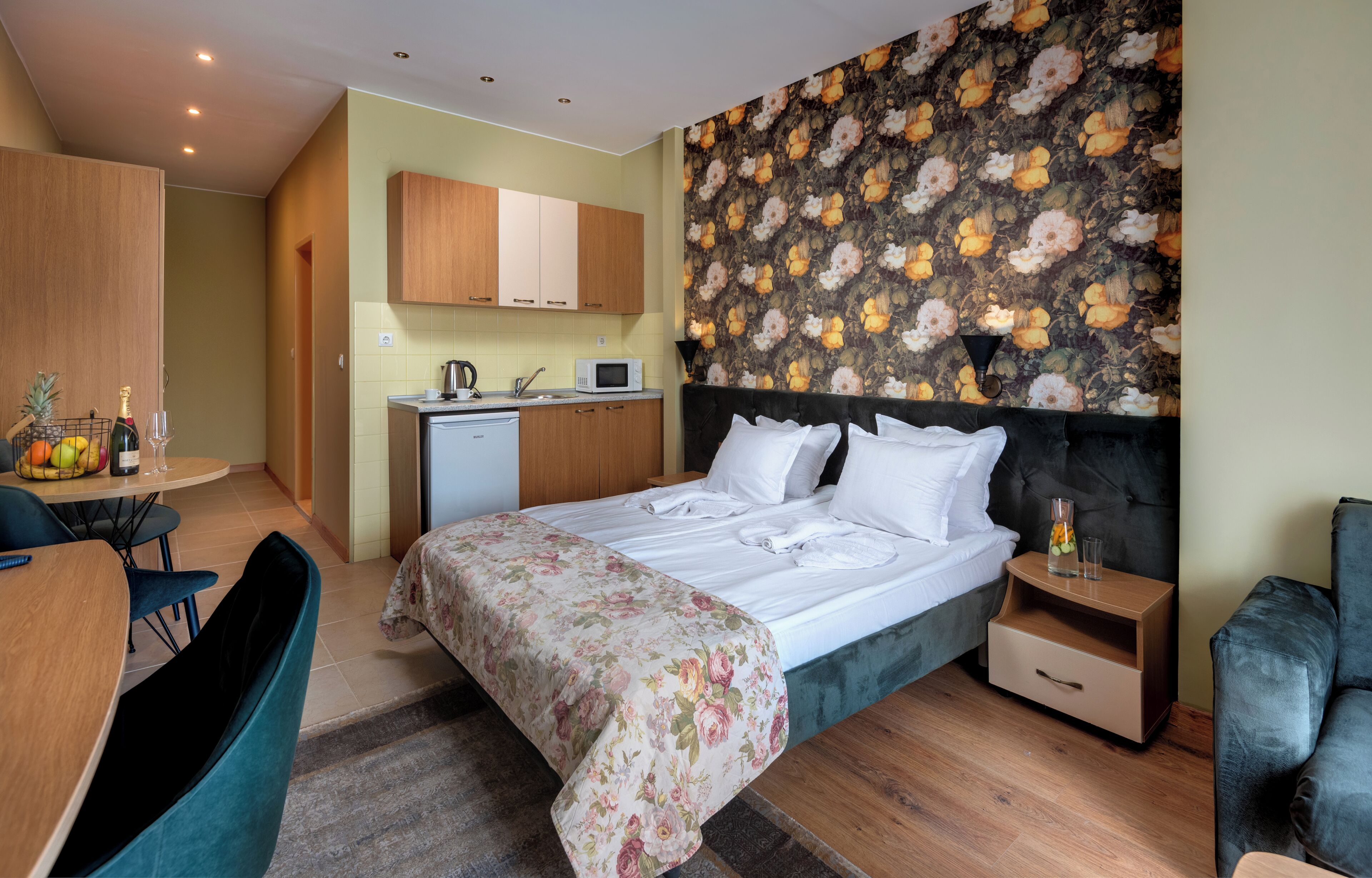 Habitación de hotel con cama, escritorio, silla, microondas y pequeña cocina.