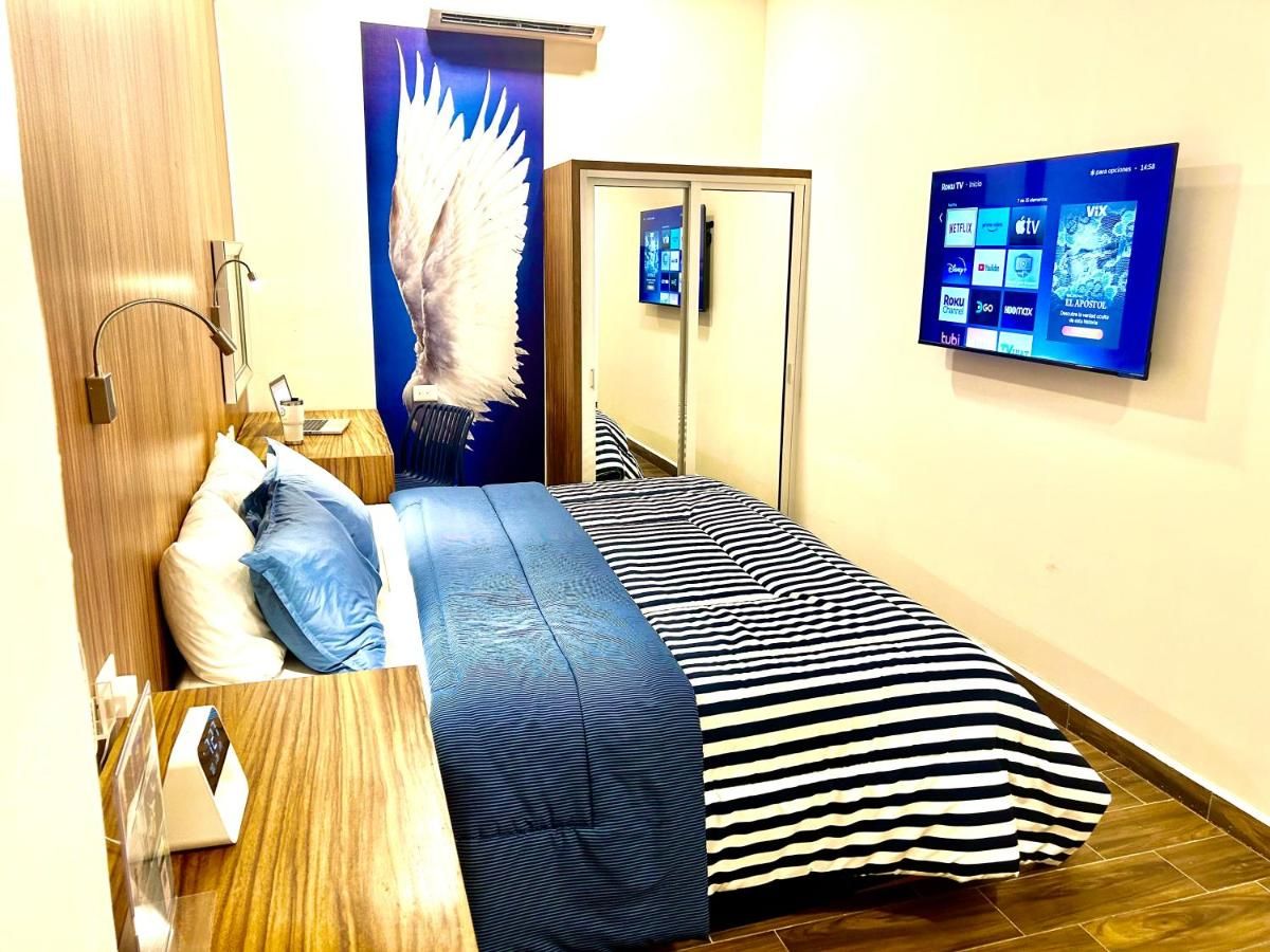 A hotel room with a bed, a desk, a mirror, and a wall-mounted TV displaying streaming services.