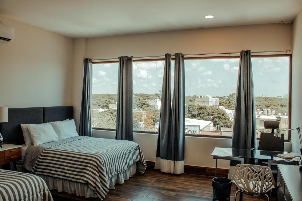 A hotel room with a large window, a bed, a desk, and a chair.