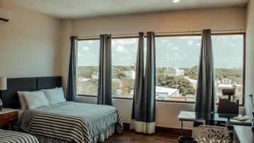 Una habitación de hotel con un ventanal grande, una cama, un escritorio y una silla.