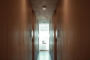 A hallway with wooden walls and a light-colored floor, leading to a door with a window. - Sky Inn Hotel (Cancun)