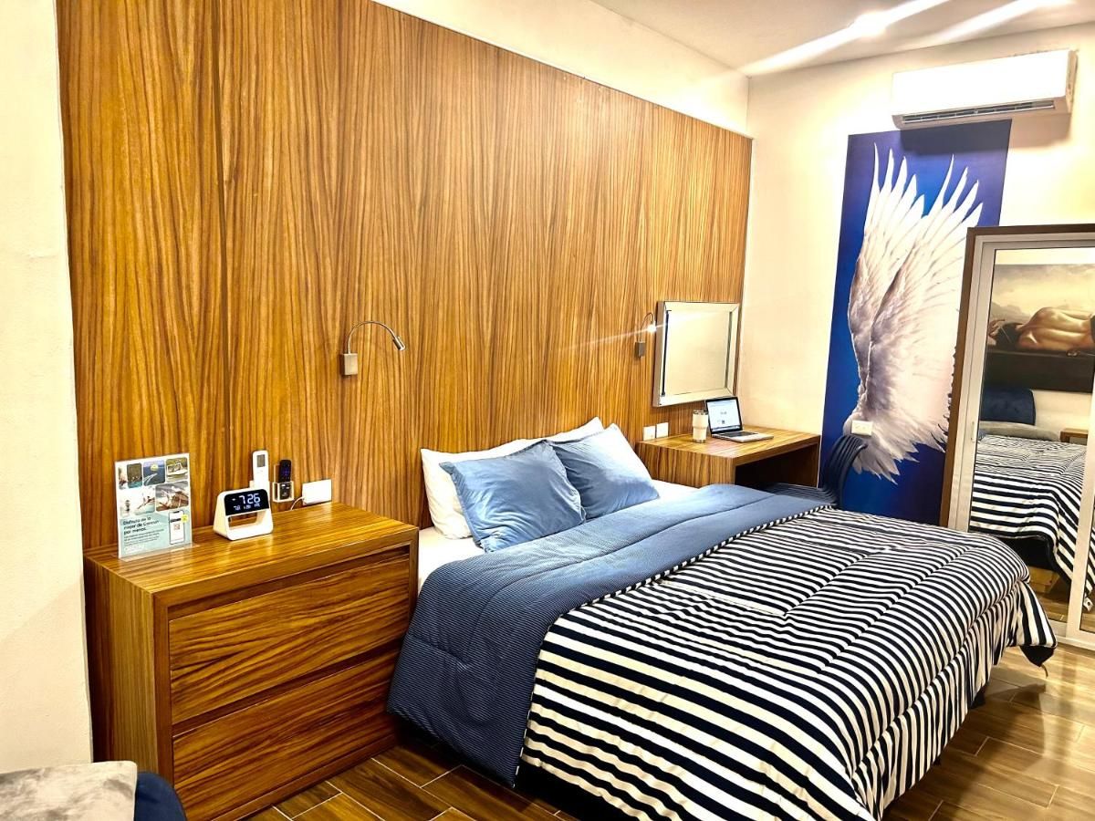 A hotel room with a wooden headboard, a bed with striped bedding, a nightstand with a clock and a photo frame, and a mirror on the wall.
