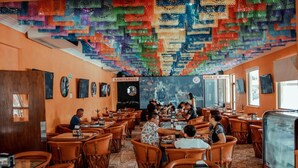 A restaurant with orange walls, wooden tables, and chairs. There are signs indicating 'SANITARIOS' and 'AREA DE NIÑOS'. - Sky Inn Hotel (Cancun)
