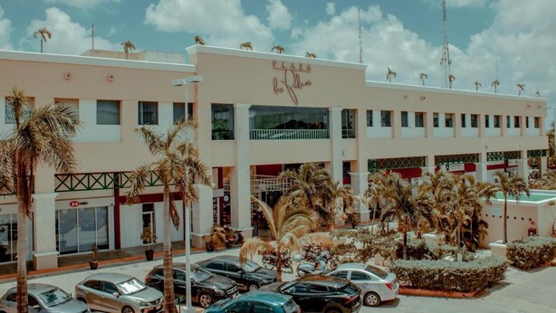 A hotel with a central atrium, palm trees, and a parking lot. - Sky Inn Hotel (Cancun)