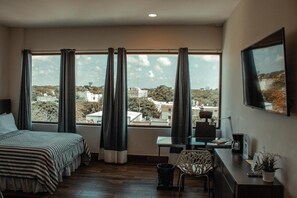 Une chambre d’hôtel équipée d’un lit, d’un bureau, d’une chaise et de grandes fenêtres donnant sur la ville.