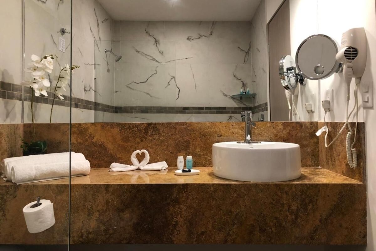 Une salle de bain avec un meuble-lavabo en marbre, un lavabo rond, un porte-serviettes, un miroir et un sèche-cheveux.