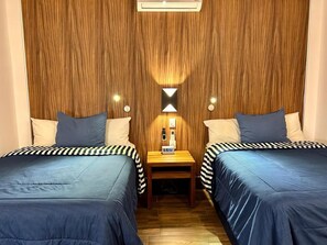 A room with two beds, each with striped bedding, a nightstand with a clock, and a wall-mounted air conditioner. - Sky Inn Hotel (Cancun)