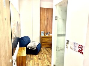 Habitación de hotel con piso de madera, un sofá azul, una mesita con una manta y un armario de madera con un reloj y un teléfono.