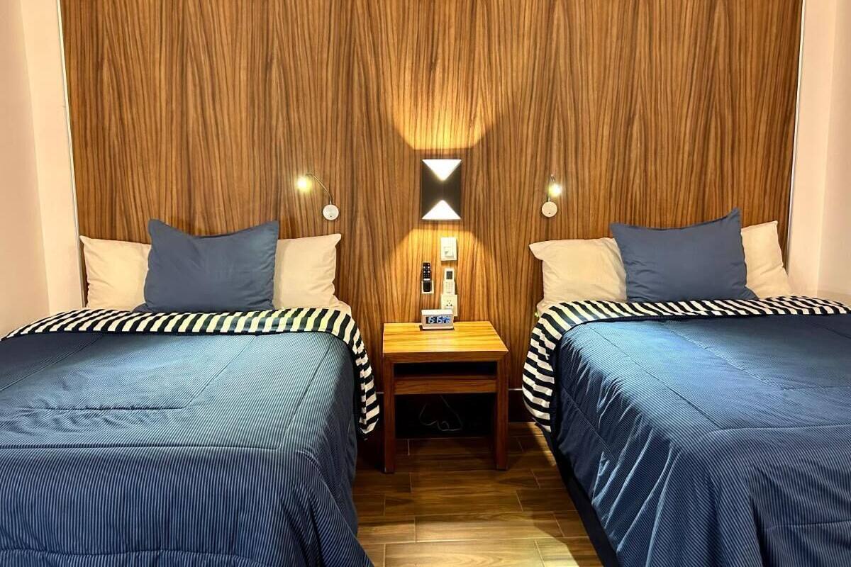 Une chambre avec deux lits, chacun doté de draps à rayures, une table de chevet avec une horloge et un climatiseur fixé au mur.