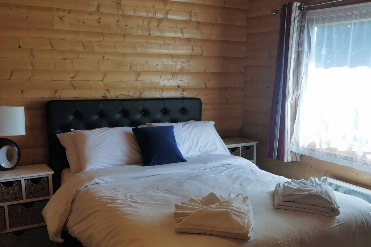 A wooden-paneled bedroom with a large bed, white bedding, a black headboard, and a bedside table with a lamp.