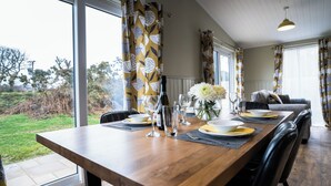 A dining area with a wooden table set for two, a bottle of wine, and a vase of flowers. - Chestnut Meadow Country Park (Bexhill-on-Sea)
