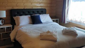 A wooden-paneled bedroom with a large bed, white bedding, a black headboard, and a bedside table with a lamp.