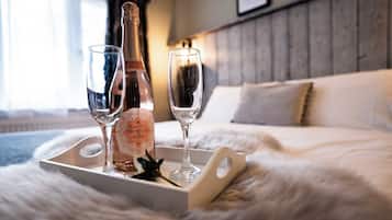 A bottle of Prosecco DOC G Rose on a tray with two champagne flutes on a fluffy white bedspread.