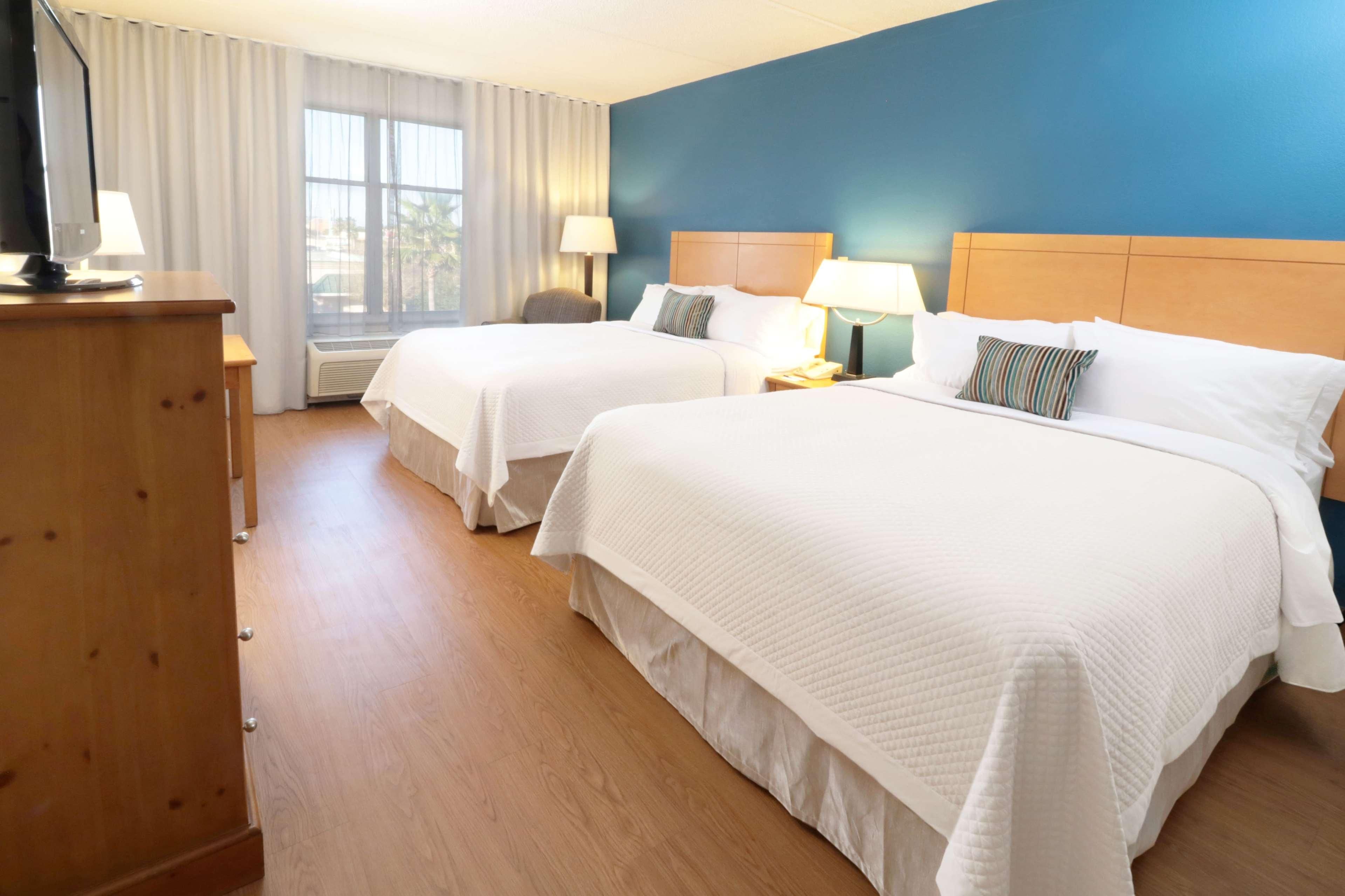 Habitación de hotel con dos camas, un aparador de madera, un escritorio con computadora y una ventana con cortinas.