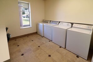 A laundry room with four white washers and dryers, a window, and a tiled floor. - Wyndham Garden Mcallen at La Plaza Mall (McAllen)
