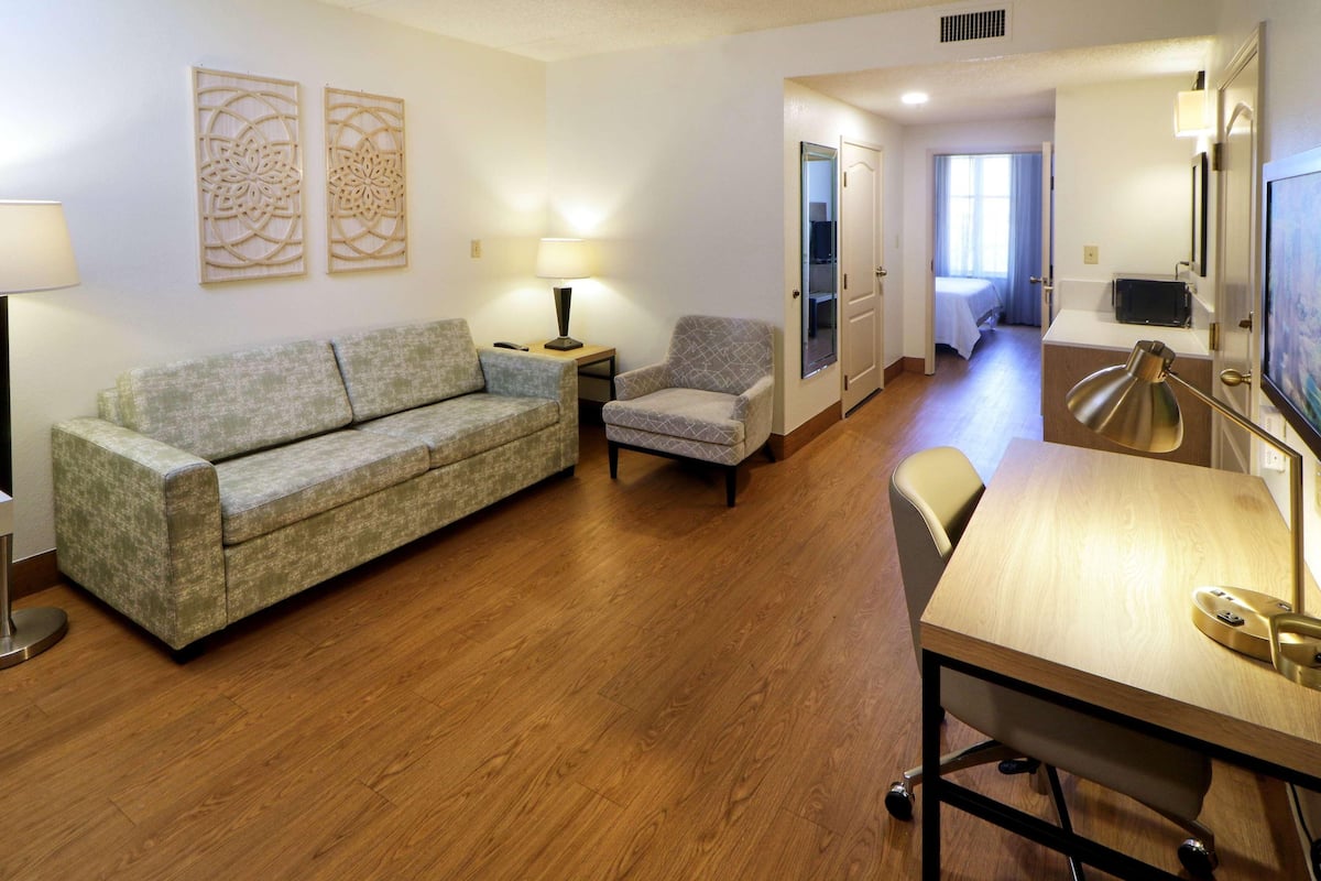 Habitación de hotel con sofá, sillón, escritorio y lámpara.