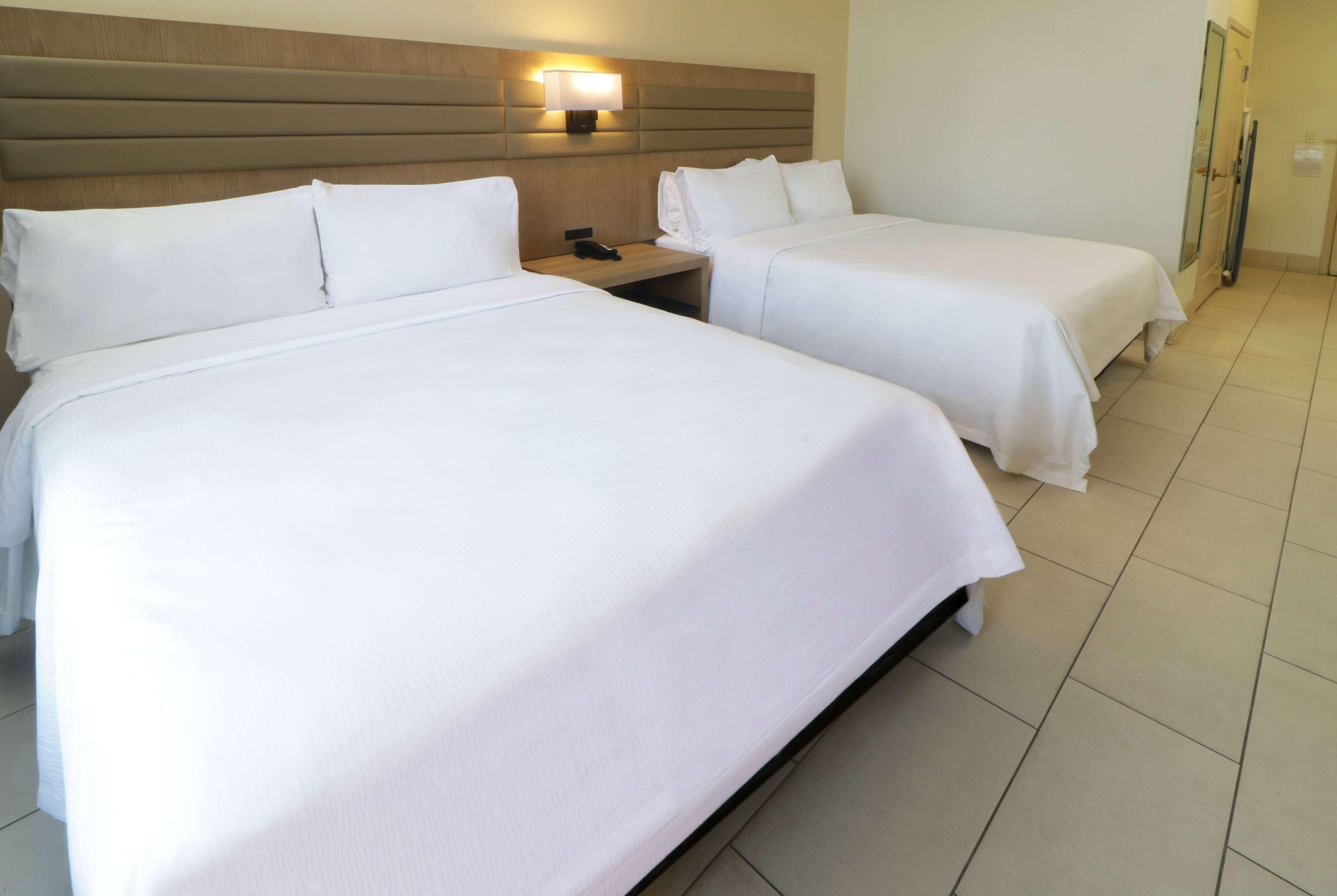 Een hotelkamer met twee eenpersoonsbedden, een nachtkastje met een telefoon en een wandlamp.