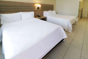 Et hotelværelse med to enkeltsenge, et natbord med en telefon og en lampe på væggen.
