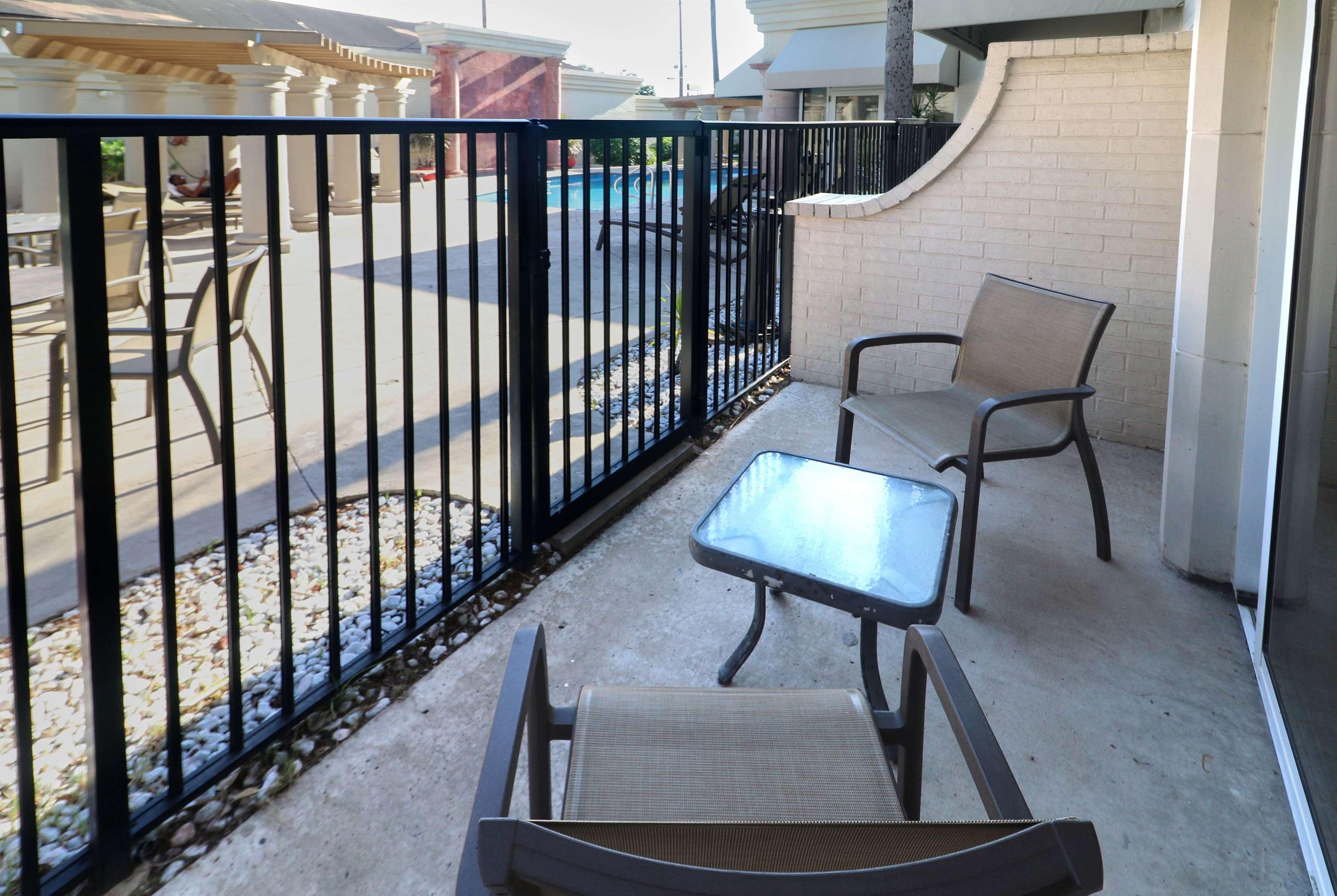 An outdoor seating area with a pool in the background, enclosed by a black metal fence.